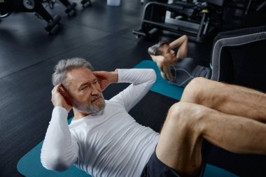 Bir adam spor salonundaki egzersiz minderinde mekik çekiyor. Fiziksel kondisyonunu ve çekirdek gücünü arttırmaya odaklanıyor.