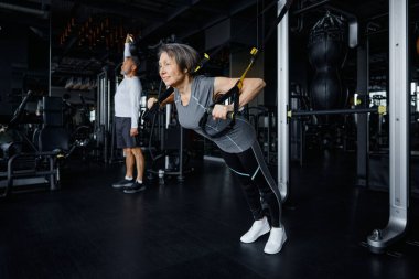 Yaşı büyük bir kadın yerel bir spor salonunda özel bir egzersiz makinesinde şınav çekiyor.