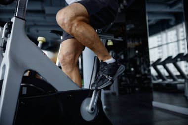 Durağan bir bisiklette bisiklet süren, spor salonundaki spor salonlarını işaretleyen, yakın çekim yapan bir adam.