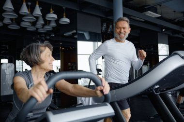 Aktif son sınıflar koşu bandında antrenman yapmaktan hoşlanırlar. Olgun kadın egzersiz bisikleti sürüyor ve erkek koşu bandında koşuyor.