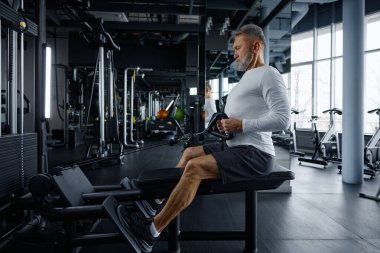 Son sınıf öğrencisi iyi donanımlı bir spor salonunda kablo makinesiyle kürek egzersizi yapıyor. Yetişkinler için spor ve dayanıklılık eğitimine odaklanın.