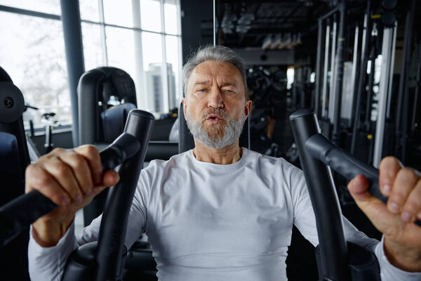 Portrait of an older man hardly training in a gym. Mature man is doing a hard exercise in a gym setting