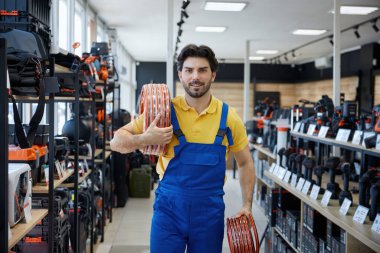 Mavi tulumla birlikte parlak sarı bir gömlek giyen bir adam elinde bir hortum tutuyor ve bir görev üzerinde çalışmaya hazır.