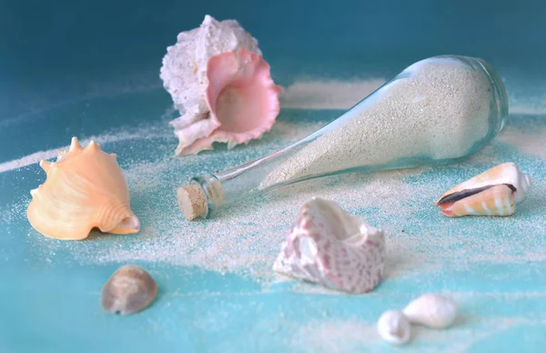 Sand in a little bottle and tropical seashells on a blue beach towel — Stock Photo, Image