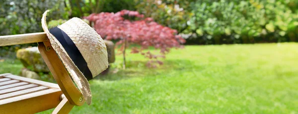 Nära på en halm hatt på ett arm stöd av en stol i en trädgård på sommaren — Stockfoto
