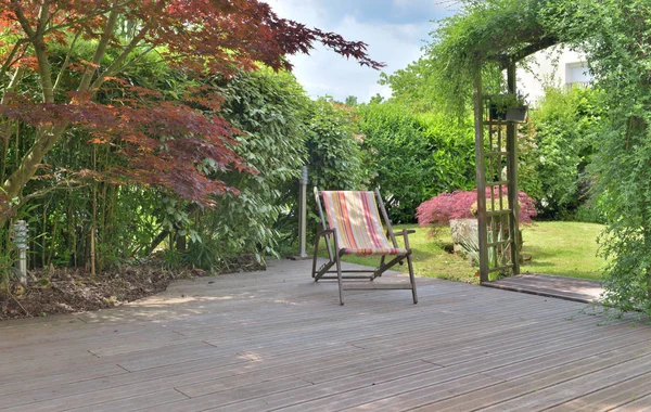 Liegestuhl auf einer Holzterrasse in einem gepflegten Garten — Stockfoto