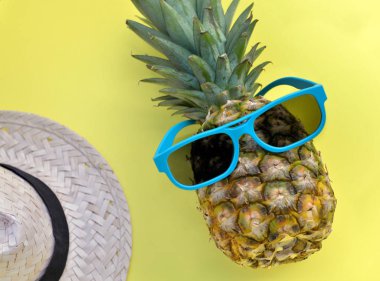 sarı arka plan üzerinde mavi güneş gözlüğü ve hasır şapka ile ananas 