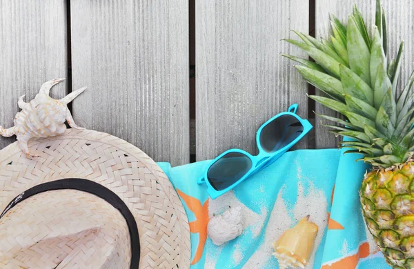 Vista superior sobre chapéu de palha, toalha de praia, óculos de sol e abacaxi no terraço de madeira — Fotografia de Stock