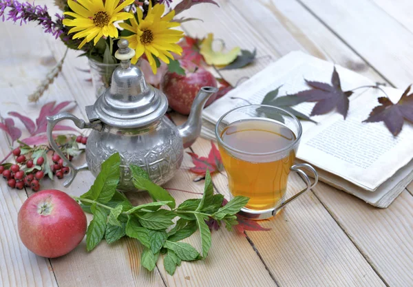 Cup of mint tea  on a garden table with flowers and book for relaxing moment in autumn — Stock Photo, Image