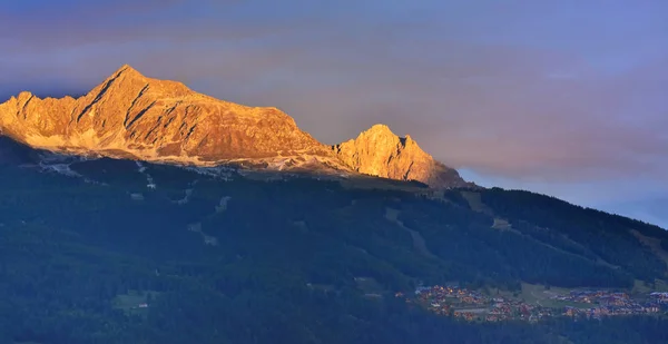 Bela montanha laranja ao pôr do sol acima da aldeia alpina — Fotografia de Stock