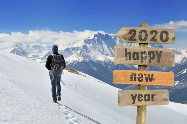 2020 gelukkig nieuwjaar wrtten op een postbord met een wandelaar wandelen op de sneeuw in een bergachtige achtergrond — Stockfoto