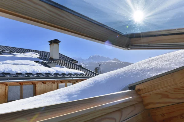 Vue depuis une fenêtre ouvrant sur un toit recouvert de neige dans un chalet alpin — Photo