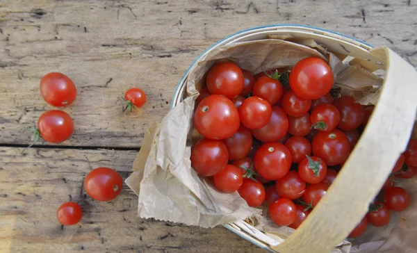 Свіжі вишневі помідори в маленькому кошику на дошці — стокове фото