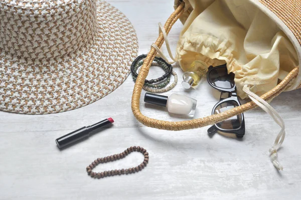 hand bag and hat with female accessories spilled on white table