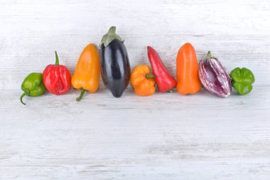 Beyaz bir masada yan yana renkli biber ve patlıcan koleksiyonu.  