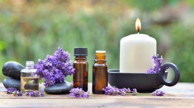 Lavanta çiçeğinin arasında mum eşliğinde, ahşap bir masa üzerine yerleştirilmiş, gerekli yağ şişeleri.