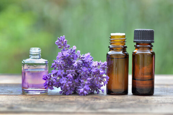 bottles of essential oil and ouquet of lavender flower arranged on a wooden table in garden 