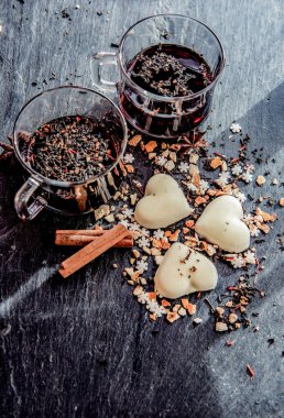  iki kadehte şarap, kalp şeklinde kurabiyeler ve baharatlar, gri bir arkaplanda dizilmiş. 