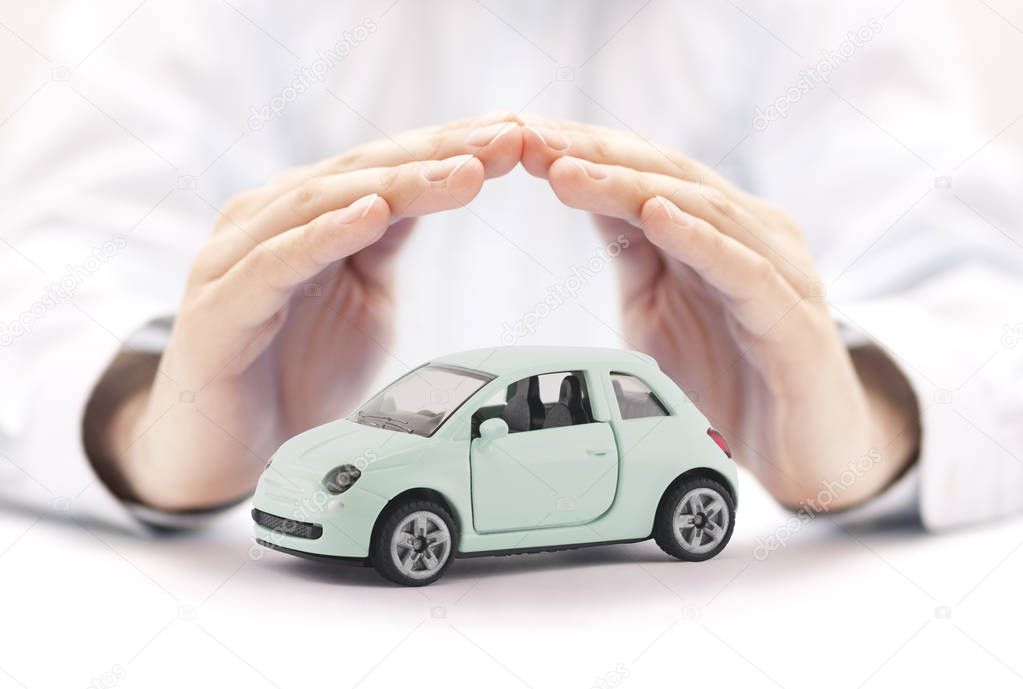 Car insurance concept. Small toy car covered by hands
