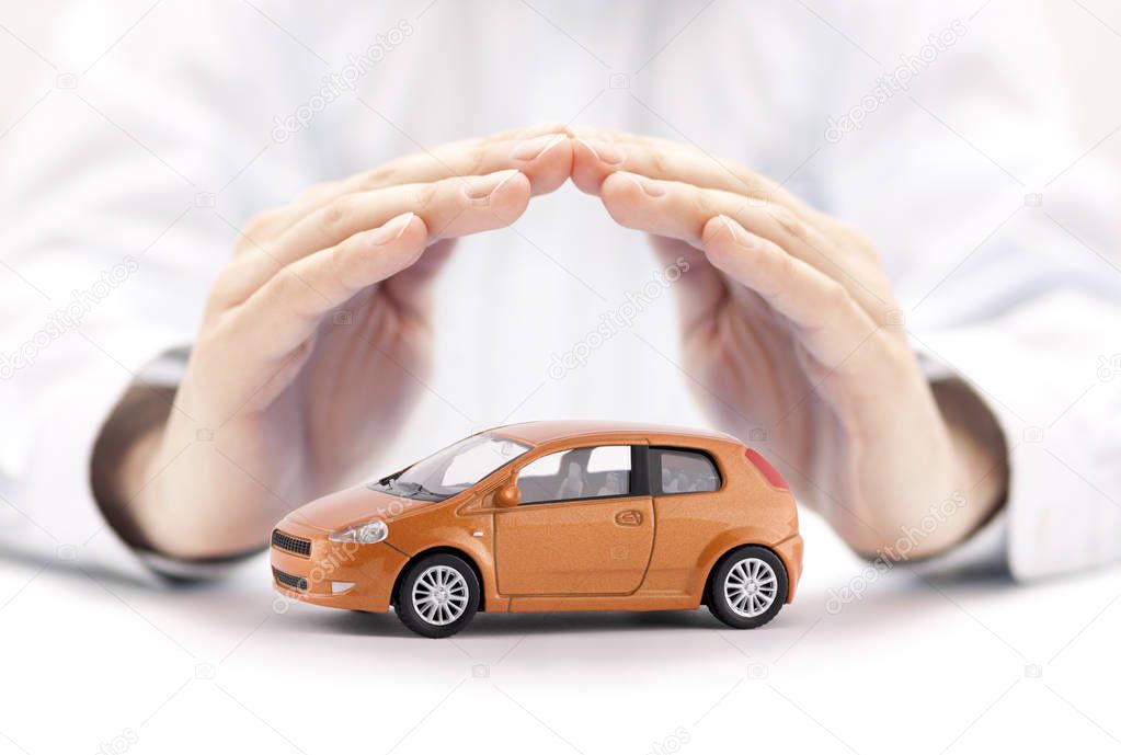 Car insurance concept. Small toy car covered by hands