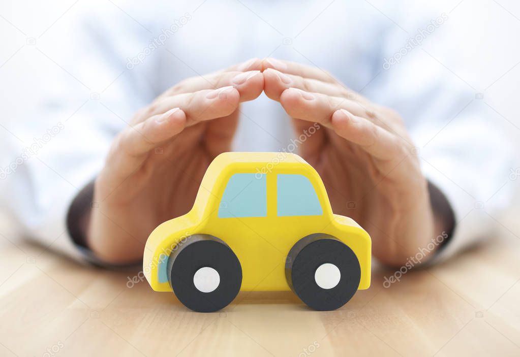 Car insurance concept. Small toy car covered by hands