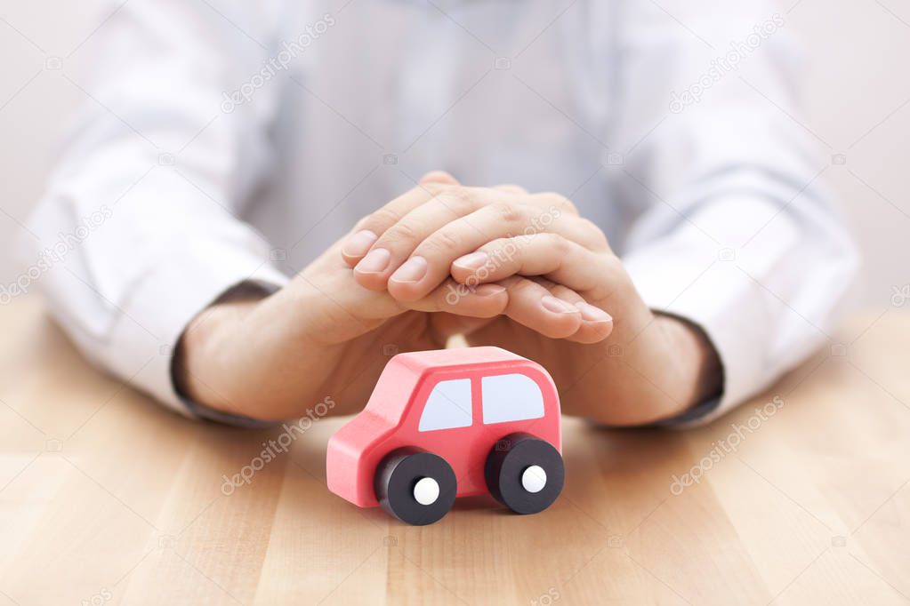 Car insurance concept. Small toy car covered by hands
