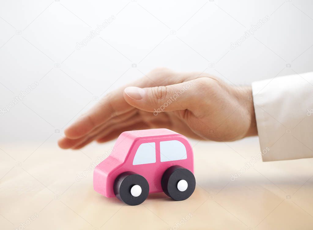 Car insurance concept. Small toy car covered by hand