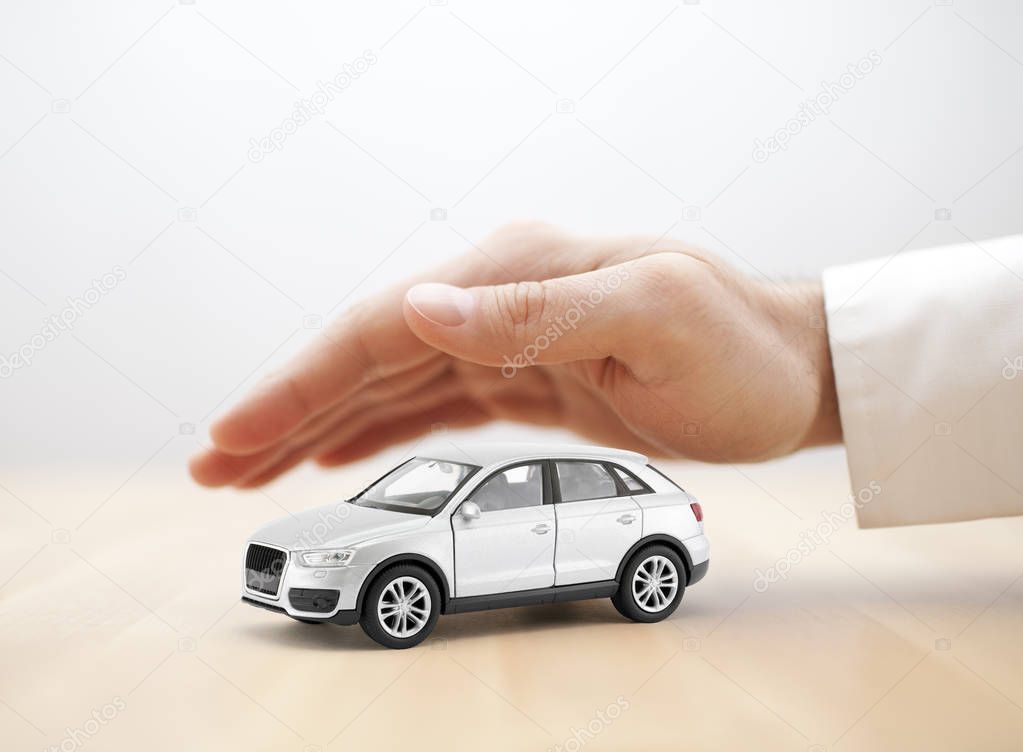 Car insurance concept. Small silver toy car covered by hand
