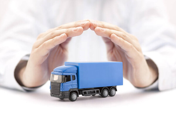 Car insurance. Blue truck miniature covered by hands. 