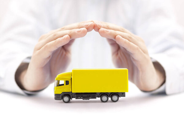 Car insurance. Yellow truck miniature covered by hands. 