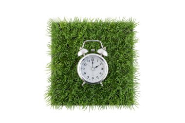 Yeşil çimen alanının karesi üzerindeki eski usul alarm saati kırpma yolu ile beyaz arkaplanda izole edildi 