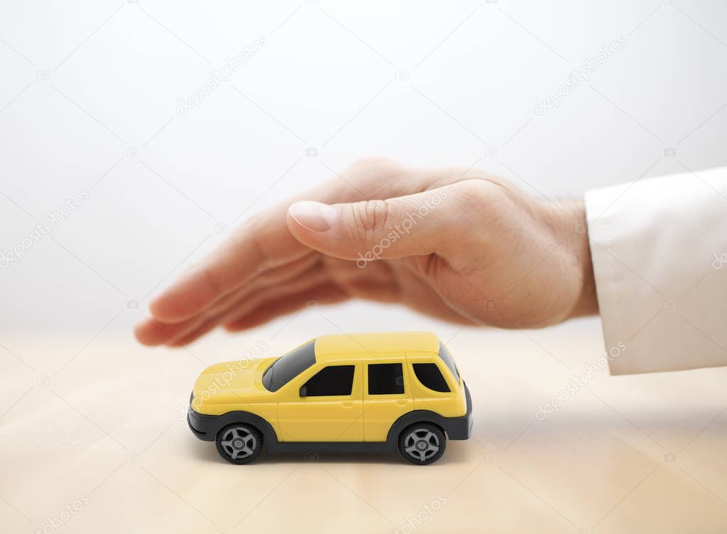 Car insurance concept with yellow car toy covered by hand 
