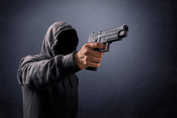 Человек в капюшоне с пистолетом в темноте