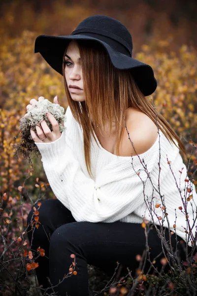 Woman sitting in the yellow bushes with a moss in hands