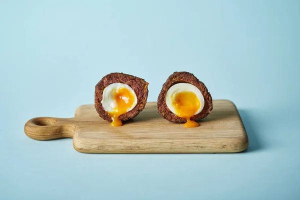 halved scotch egg with runny egg yolk on cutting board