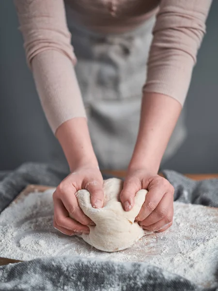 Woman hands kneading a bread dough on a wooden board
