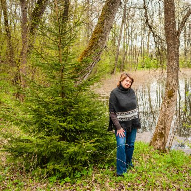 Orta yaşlı kadın parkta gölet tarafından panço, dinlenme