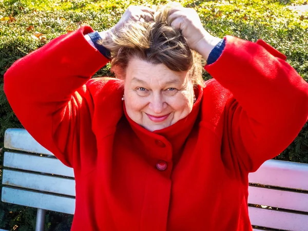 Женщина средних лет в красном пальто отдыхает в парке — стоковое фото