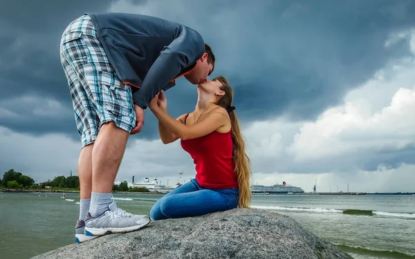 Девушка в красном и парень целуется на большом камне — стоковое фото