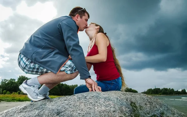 Girl in red and guy kissing on a big rock — Stock Photo, Image