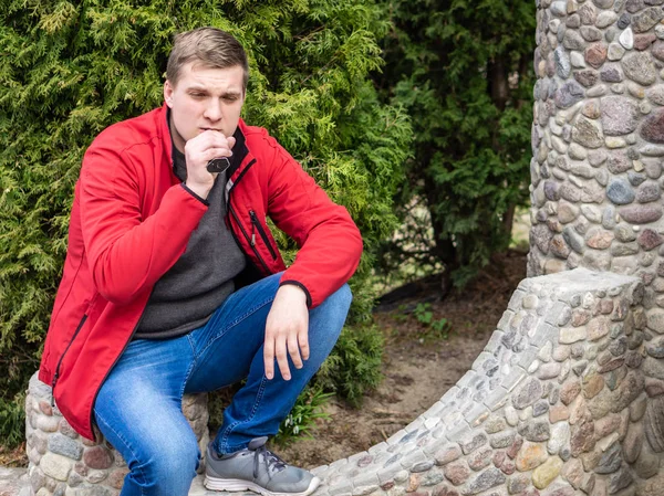 Un joven con chaqueta roja fuma un cigarrillo electrónico — Foto de Stock