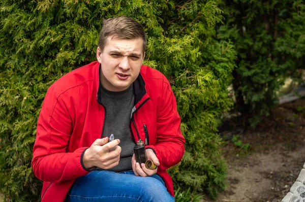Ein junger Mann in roter Jacke raucht eine elektronische Zigarette — Stockfoto