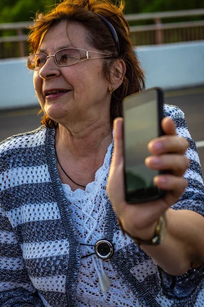 Stařena v brýlích s mobilním telefonem na ulici — Stock fotografie