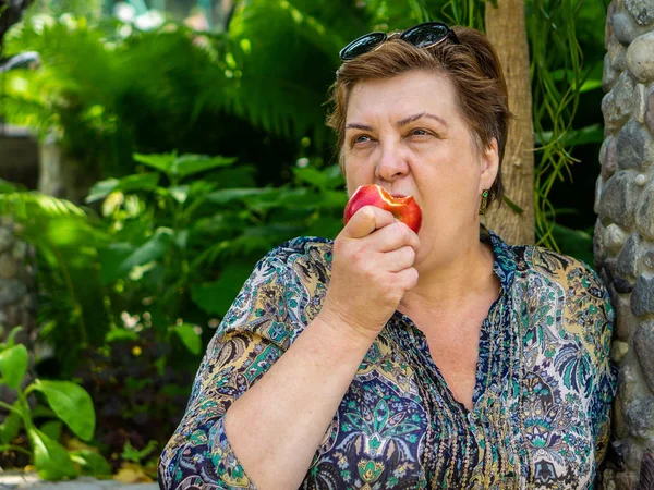 Зрелая женщина отдыхает и ест красное яблоко — стоковое фото