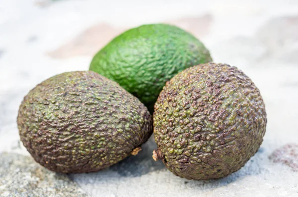 Drie vruchten van avocado liggen op een stenen tafel — Stockfoto