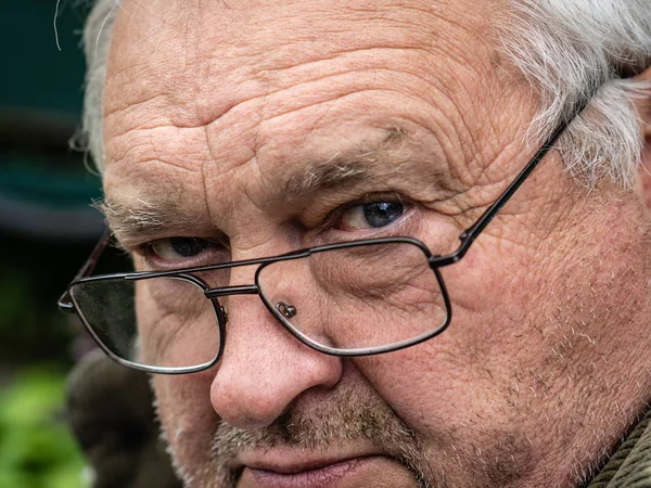 Pensive oude grootvader in vuile bril kijkt in de voorkant van hem — Stockfoto