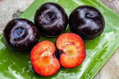 Üç koyu mor erik meyve ve bir yeşil plaka üzerinde kesilmiş