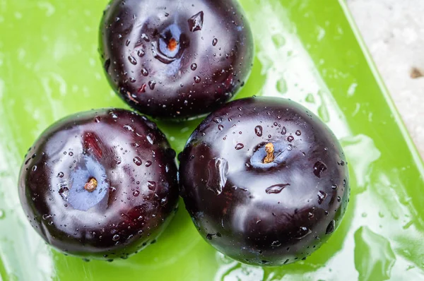 Drei dunkelviolette Pflaumenfrüchte auf einem grünen Teller — Stockfoto