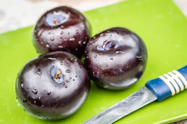 Три темно-фиолетовых сливовых фрукта и один порез на зеленой тарелке — стоковое фото