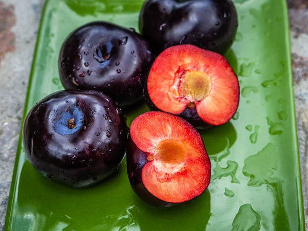 Tre mörklila plommon frukter och en klippa på en grön tallrik — Stockfoto
